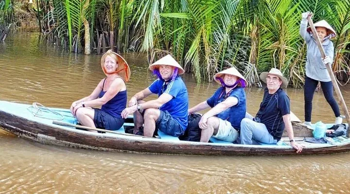Travelers in conical hats on a sampan along a palm-lined canal on a 9-day Vietnam tour package from south to north, Mekong Delta, Vietnam